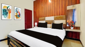A hotel room with a large bed, a wooden accent wall, a red door, and two framed artworks on the wall. - Hotel O Singanallur Railway Junction (Coimbatore)