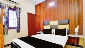 A hotel room with a bed, a window with curtains, a wooden wall panel, a bedside table with a lamp, and a red door. - Hotel O Singanallur Railway Junction (Coimbatore)
