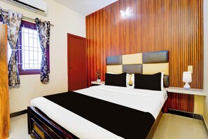 Ein Hotelzimmer mit Bett, einem Fenster mit Vorhängen, einer Holzwandverkleidung, einem Nachttisch mit Lampe und einer roten Tür.