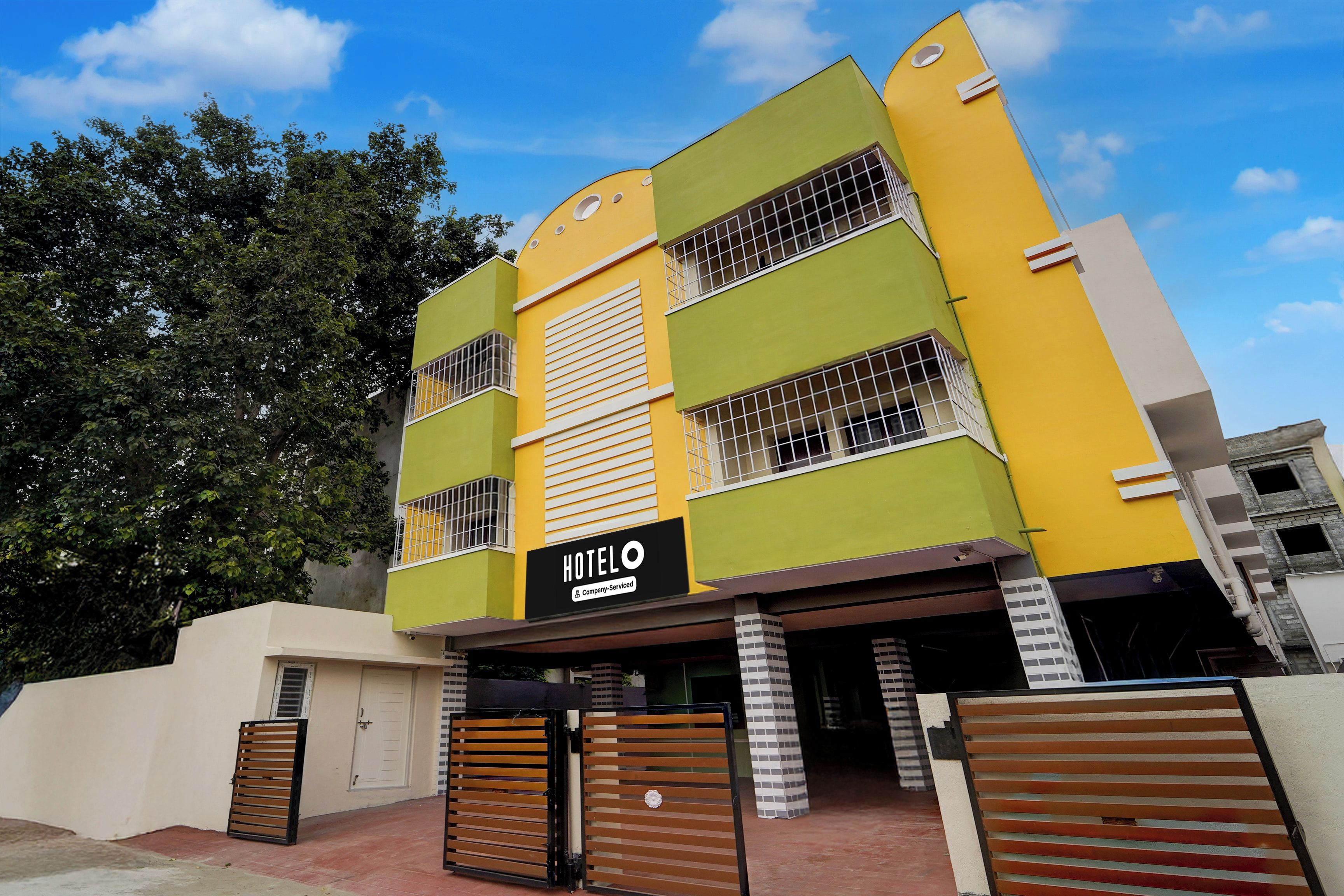 Um hotel de vários andares com fachada verde e amarela, uma placa indicando que oferece serviços corporativos, e uma entrada com portão.