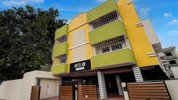 Um hotel de vários andares com fachada verde e amarela, uma placa indicando que oferece serviços corporativos, e uma entrada com portão.