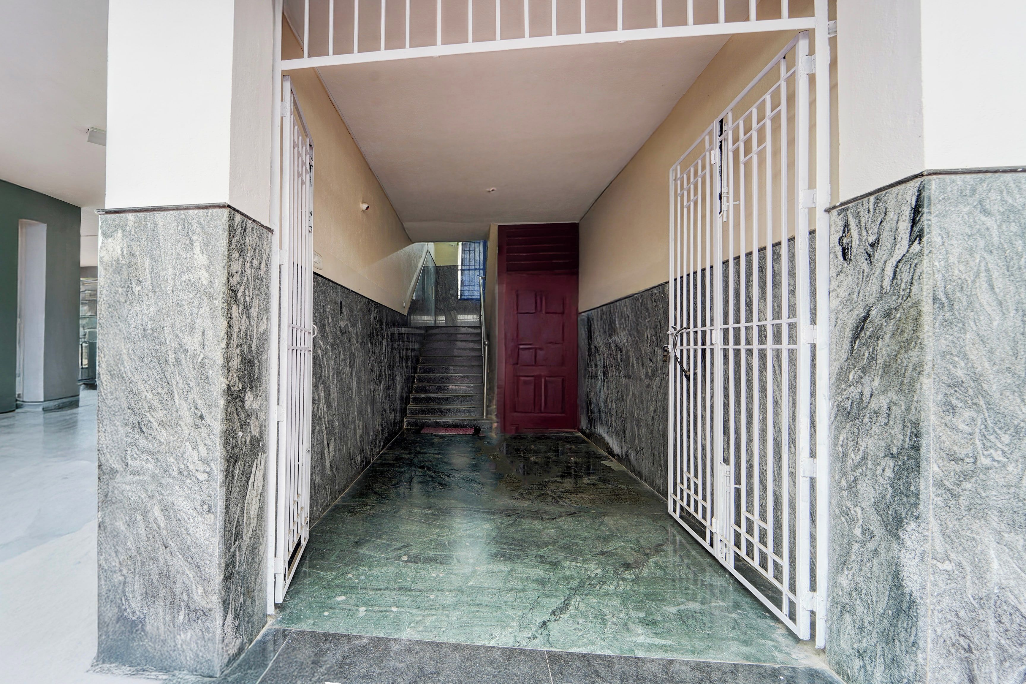 Corredor com paredes de mármore e um portão de metal, que dá acesso a uma escadaria.
