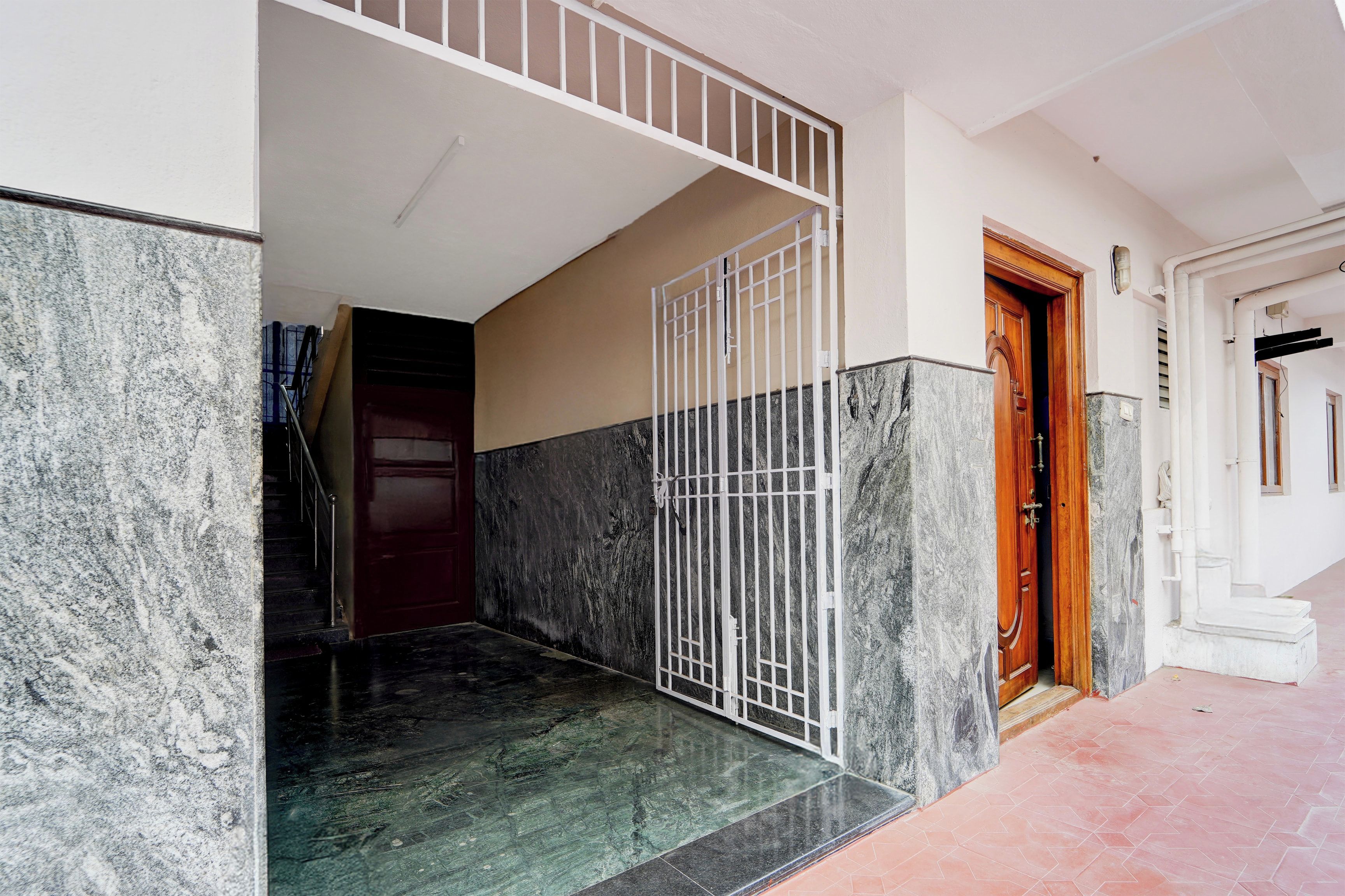 Entrada de um edifício com porta protegida por grades, escadaria e piso de azulejos.