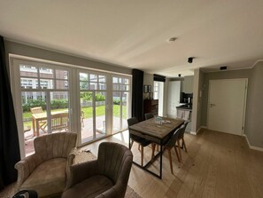 Un vaste salon doté d’une grande porte-fenêtre coulissante donnant sur un patio, un coin repas avec une table en bois et un espace cuisine.