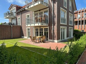 A multi-story residential building with a brick facade, balconies, and a patio area with outdoor furniture. - Holiday Apartment With 1 Bedroom (Wangerooge)