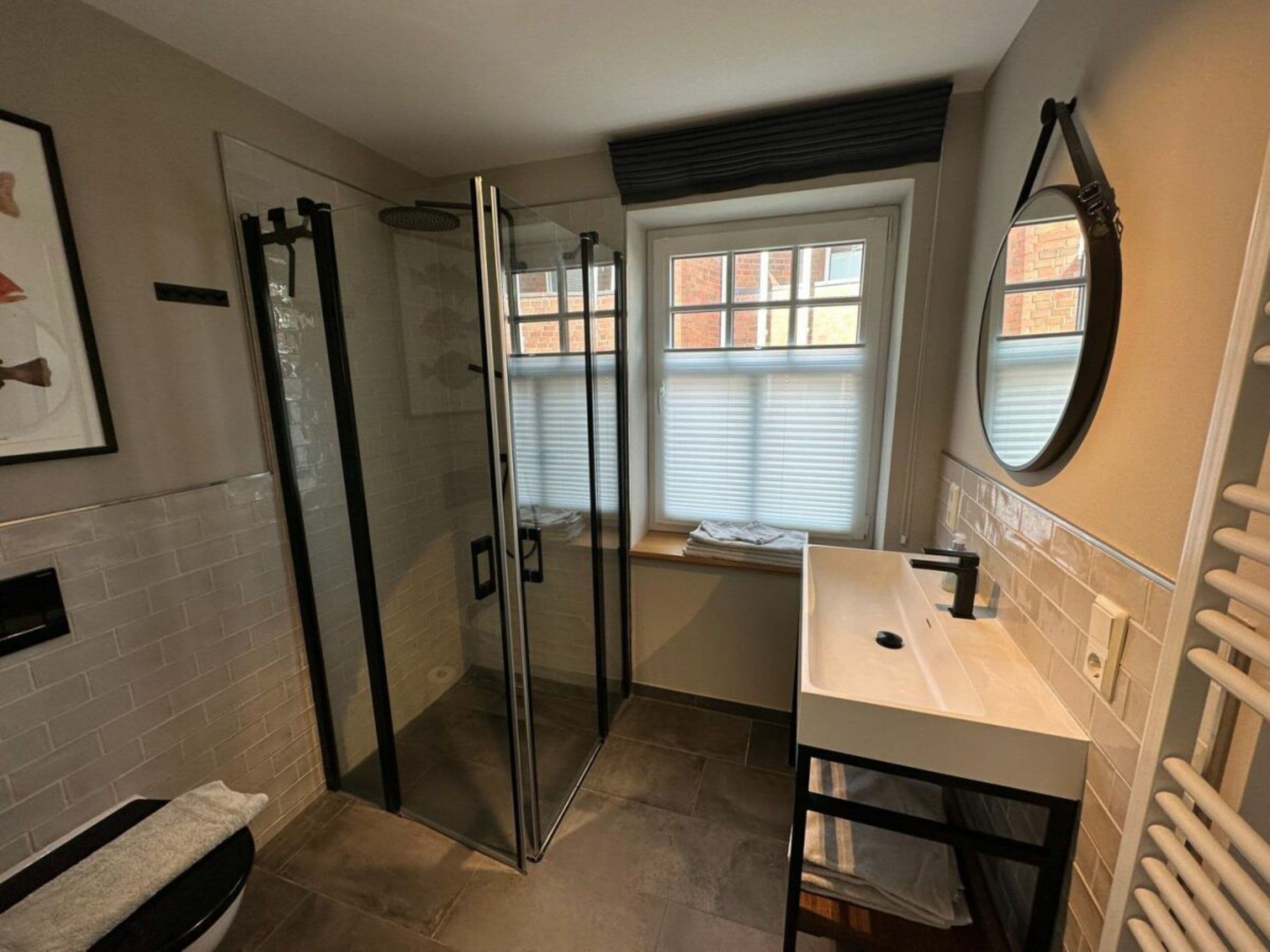 A bathroom with a glass-enclosed shower, a white sink, and a window with blinds.