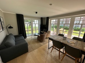 Un salon comprenant un canapé, une table à manger avec des chaises, un téléviseur et de grandes fenêtres.