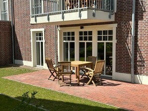 A patio with a wooden table and chairs, a brick pathway, and a building with a brick facade and large windows. - Holiday Apartment With 1 Bedroom (Wangerooge)