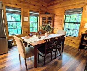 A wooden interior with a dining table, chairs, a vase with flowers, and a cabinet with glass doors. - Rest & Unwind at Mountain Laurel Retreat 3-BR cabin in charming Sautee Nacoochee (Sautee Nacoochee)