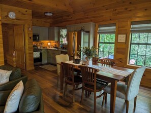 A wooden interior with a dining table, chairs, a sofa, and a kitchen area. - Rest & Unwind at Mountain Laurel Retreat 3-BR cabin in charming Sautee Nacoochee (Sautee Nacoochee)