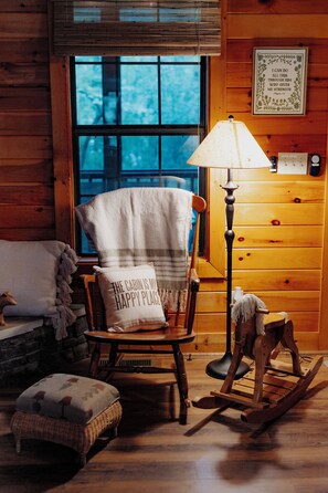 A cozy cabin interior with a rocking chair, a lamp, and a window with a view. - Rest & Unwind at Mountain Laurel Retreat 3-BR cabin in charming Sautee Nacoochee (Sautee Nacoochee)