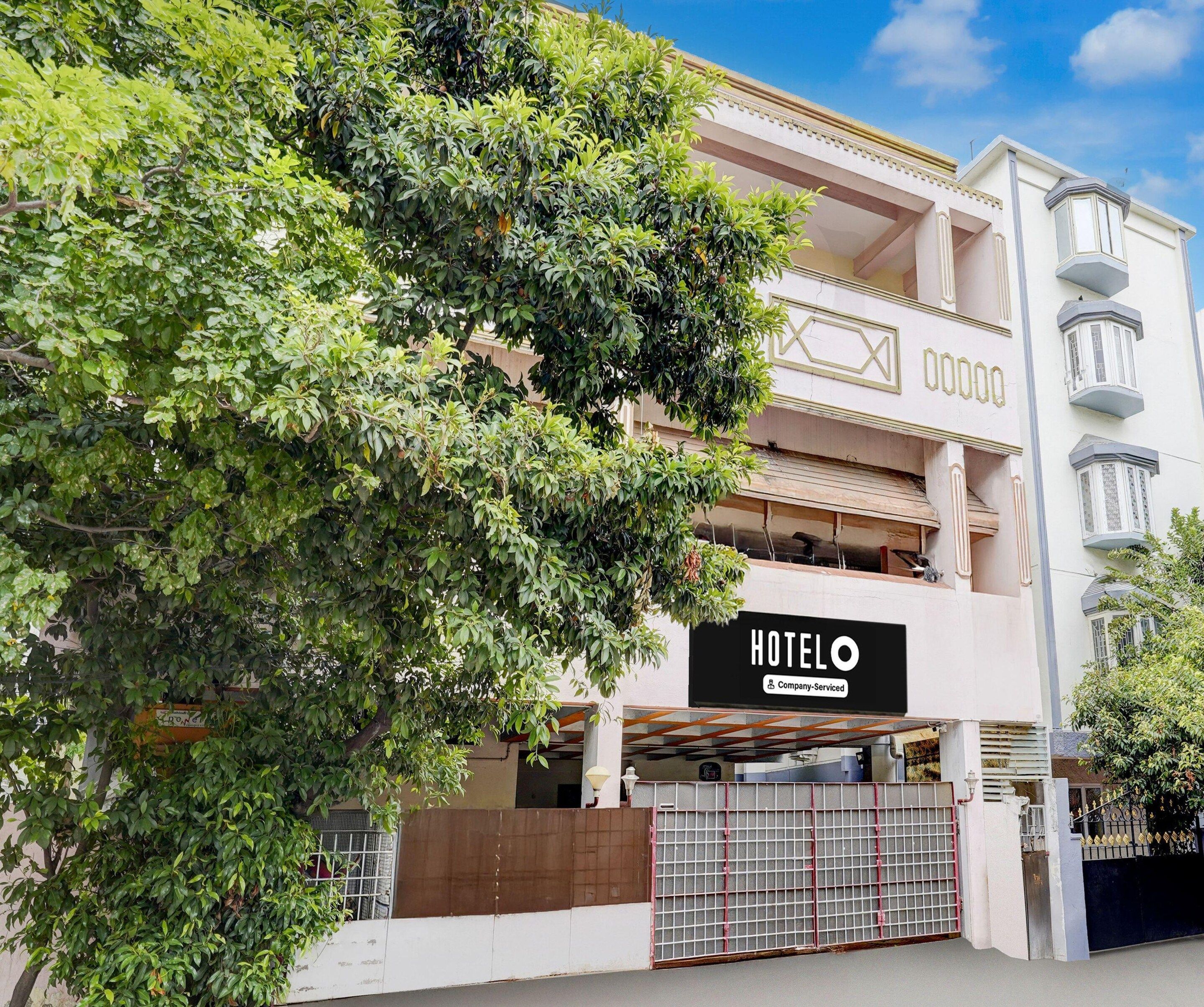 A hotel with a sign indicating it is company-serviced, a gated entrance, and a large tree in the foreground.