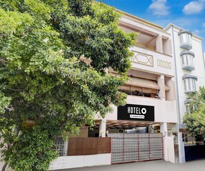 A hotel with a sign indicating it is company-serviced, a gated entrance, and a large tree in the foreground. - Premium Ambience Home (Chennai)