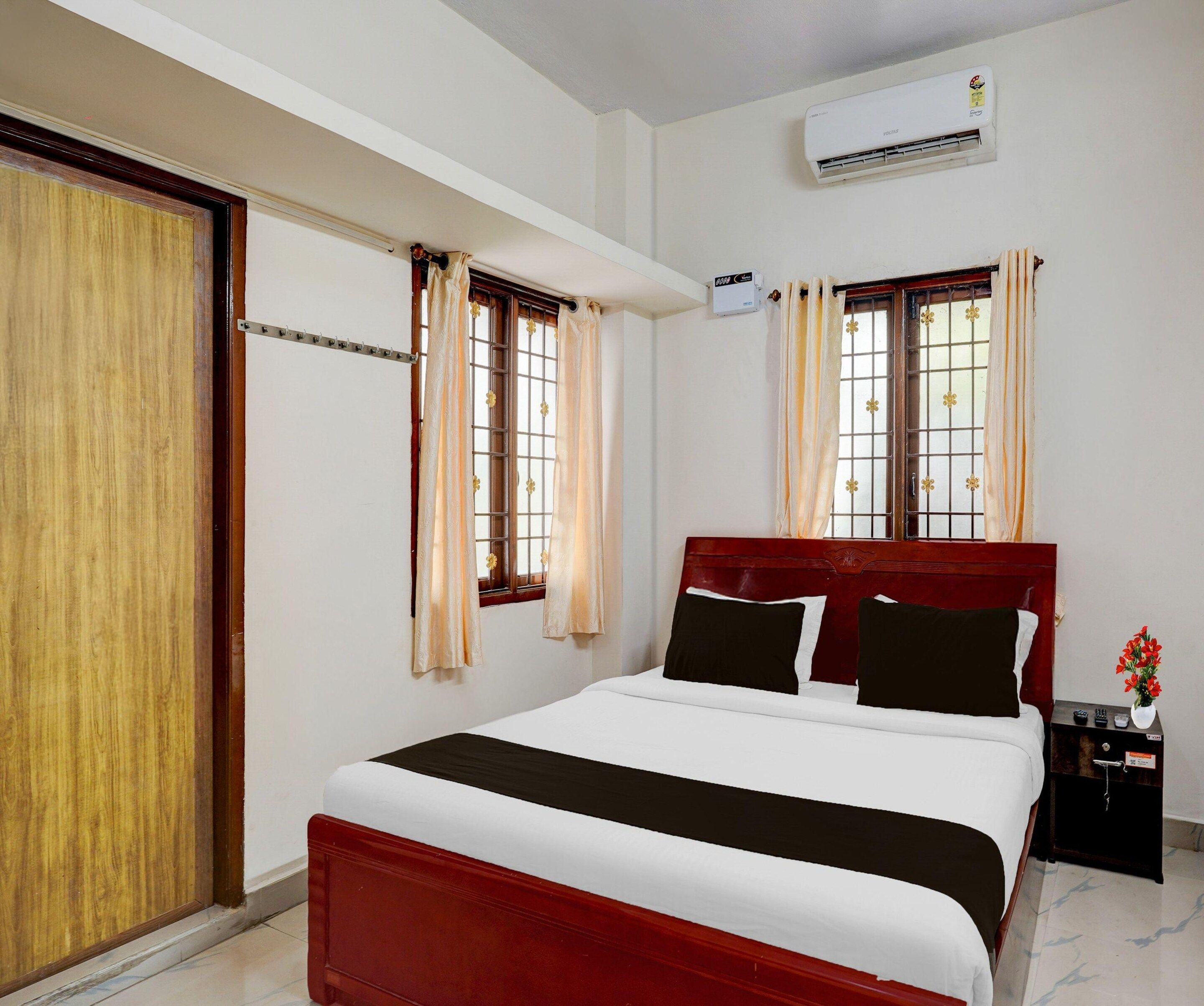 A hotel room with a bed, curtains, an air conditioning unit, a nightstand, and a window with a view.