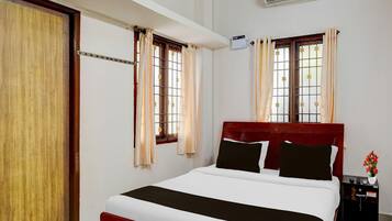 A hotel room with a bed, curtains, an air conditioning unit, a nightstand, and a window with a view.