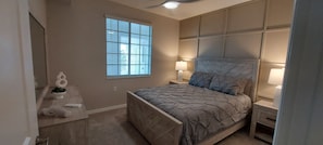 Quarto com cama, luminárias de cabeceira, uma janela e uma prateleira na parede com objetos decorativos.