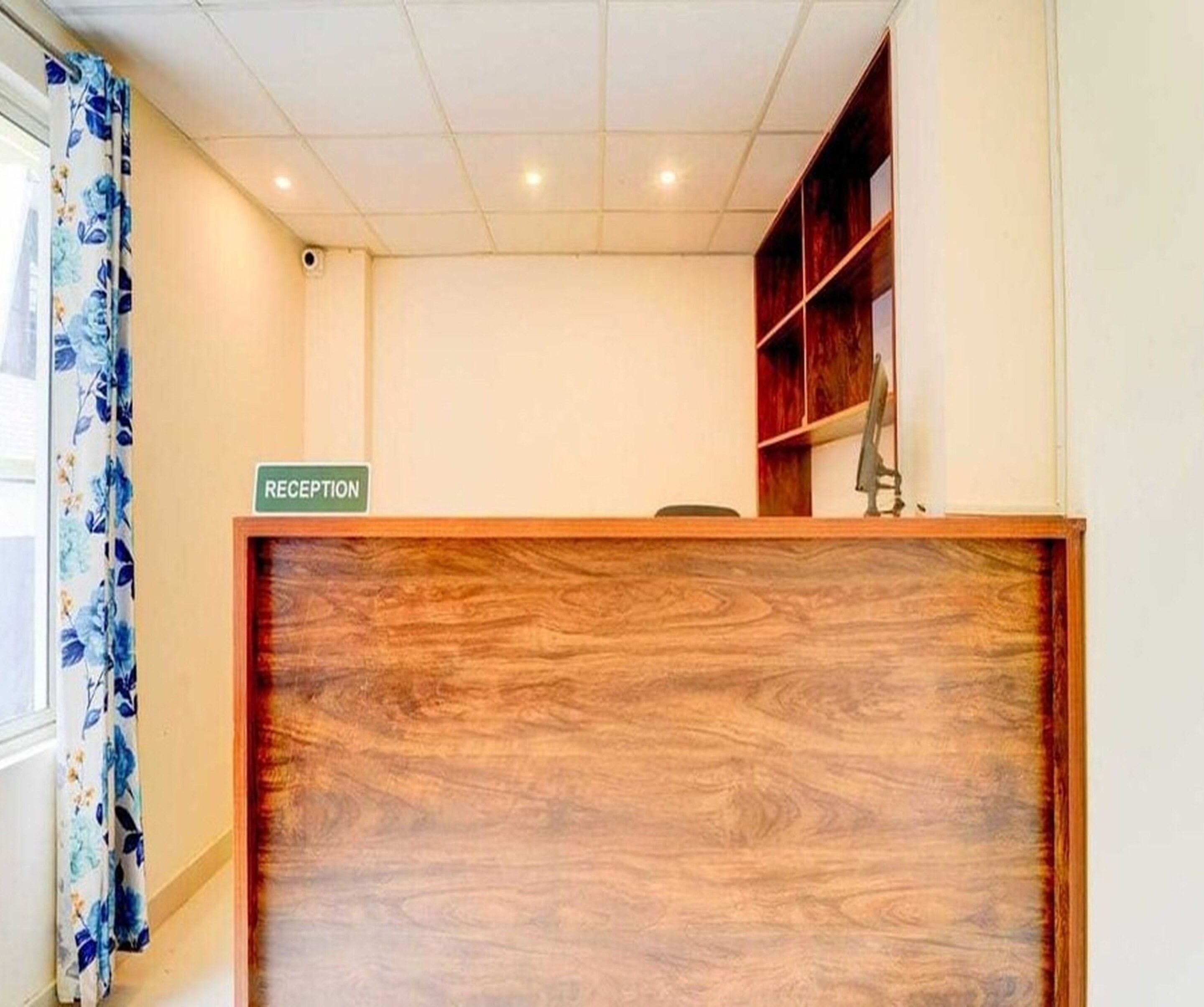 A reception desk with a sign, a wooden panel, and a window with curtains.