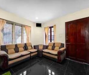 A living room with a sectional sofa, a wooden door, and large windows with curtains. - Deluxe Room Sba's Park Inn (Coimbatore)
