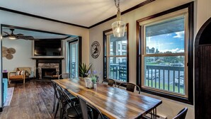 Uma sala de jantar espaçosa com uma mesa de madeira comprida, cadeiras pretas e vista para o exterior através de grandes janelas.