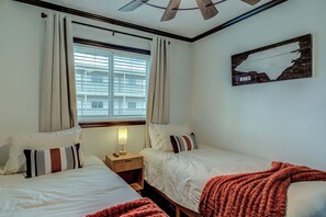 Ein Hotelzimmer mit zwei Betten, einem Fenster mit Jalousien, einem Deckenventilator, einem Nachttisch mit Lampe und einem an der Wand befestigten Schild.