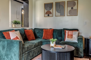 Ein Wohnzimmer mit einem grünen Sofa, mehreren Kissen, einem Couchtisch und abstrakter Wandkunst.