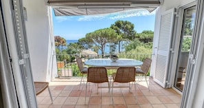 A balcony with a table and chairs, overlooking a coastal area with trees and the sea. - Rustic-modern style apartment with sea views (Calella de Palafrugell)