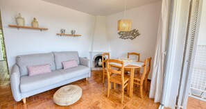 A living room with a grey sofa, wooden dining table, and chairs, a fireplace, and a hanging light fixture. - One-bedroom apartment with sea views (Calella de Palafrugell)