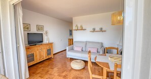 Ein Wohnzimmer mit einer Couch, einem Holz-TV-Schrank und einem Essbereich mit Tisch und Stühlen.