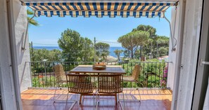 Ein Balkon mit Tisch und Stühlen mit Blick auf eine Küstenlandschaft mit Bäumen und dem Meer.