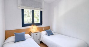 A room with two single beds, a nightstand with a lamp, and a window with a view of greenery. - Three bedroom apartment with sea view (Calella de Palafrugell)