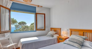A bedroom with two beds, a window with a view, a bedside table with a lamp, and a wooden headboard. - Two-bedroom apartment with sea views (Calella de Palafrugell)