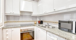 A kitchen with white cabinets, a granite countertop, a built-in oven, a microwave, and a sink. - Two-bedroom apartment with sea views (Calella de Palafrugell)