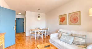 Ein Wohnzimmer mit einer Couch, einem Esstisch mit Stühlen, einem Holz-Couchtisch und einer Deckenleuchte.