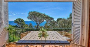A wooden table with a potted plant on a balcony overlooking a coastal view with trees and the sea. - Two-bedroom apartment with sea views (Calella de Palafrugell)