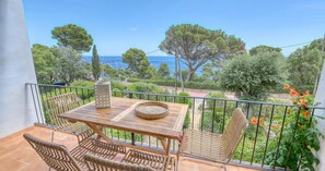 Ein Balkon mit Tisch und Stühlen mit Blick auf eine Küstenlandschaft mit Bäumen und dem Meer.