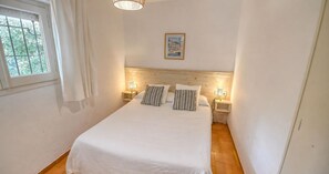Ein Schlafzimmer mit einem großen Bett, zwei Nachttischen mit Lampen, einem Fenster mit Vorhängen und einem gerahmten Bild an der Wand.