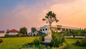Uma estátua em um jardim bem cuidado, com um edifício moderno ao fundo.