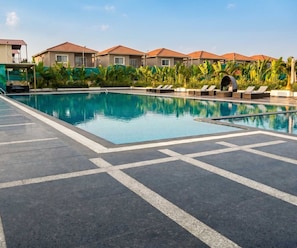 A swimming pool with lounge chairs and a covered seating area, surrounded by buildings with red roofs.