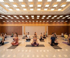 Un grupo de personas sentadas sobre esterillas de yoga en una sala amplia con techo alto e iluminación empotrada.