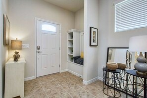 A hallway with a white door, a built-in shelf unit, a small seating area, and a table with decorative items. - 5BR Mario-themed home near Disney | Pool & Spa (Kissimmee)