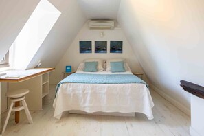 A bedroom with a sloped ceiling, a bed with a blue and white bedspread, a desk with a chair, and a small table with a lamp. - Charming house with a pool, magnificent views of the valley and Beynac Castle (Beynac-et-Cazenac)