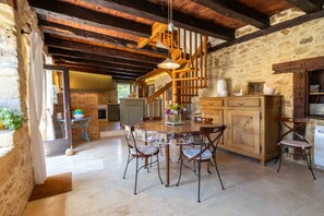 A rustic kitchen with a wooden table and chairs, a staircase, and stone walls. - Charming house with a pool, magnificent views of the valley and Beynac Castle (Beynac-et-Cazenac)