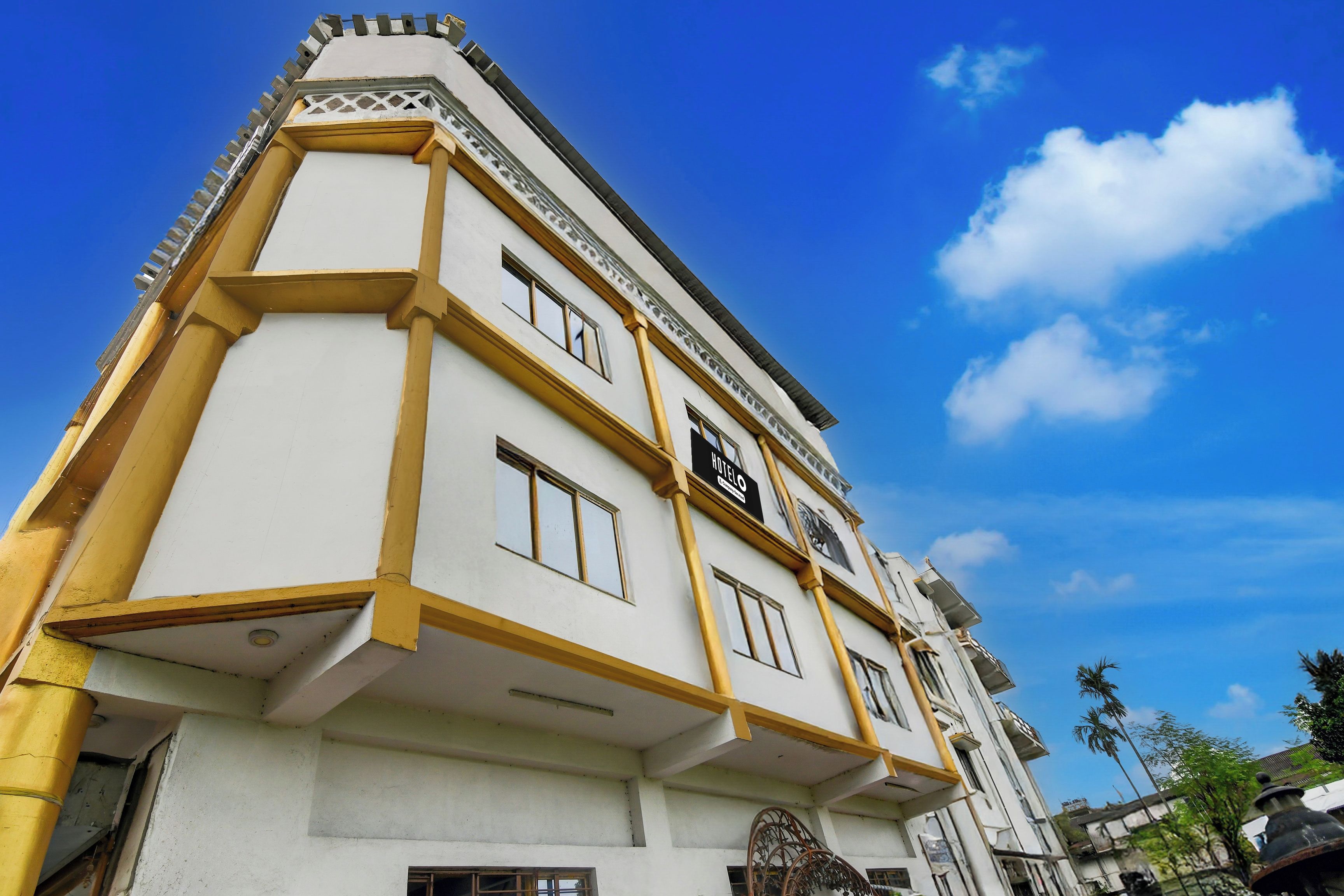 Un hôtel à la façade blanche et aux ornements jaunes, doté de nombreuses fenêtres et d’une enseigne indiquant qu’il s’agit d’un hôtel.