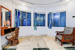 Una habitación con piso de mármol, una silla de madera, un estante de madera con un jarrón y tres ventanas con cortinas azules.