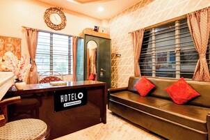 Zona de recepción de un hotel con un mostrador, un sofá con cojines rojos y un reloj de pared.
