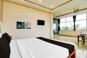 Una habitación de hotel con cama, televisión, obras de arte en la pared y vistas al exterior por la ventana.