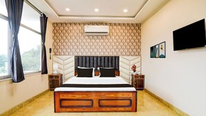 Una camera d'albergo con un letto, una TV, un condizionatore d'aria a parete e una finestra con tende.
