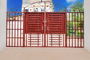Una reja metálica roja con barras verticales y un cierre central, que da acceso a un edificio con fachada blanca y ventanas azules.