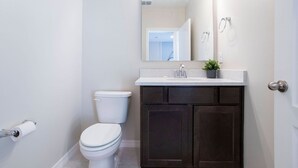Ein Badezimmer mit einer weißen Toilette, dunklen Holzsäschränken, einer weißen Arbeitsplatte und einem Spiegel über dem Waschbecken.