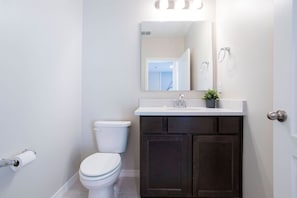 Un baño con un inodoro blanco, armarios de madera oscura, encimera blanca y un espejo sobre el lavamanos.